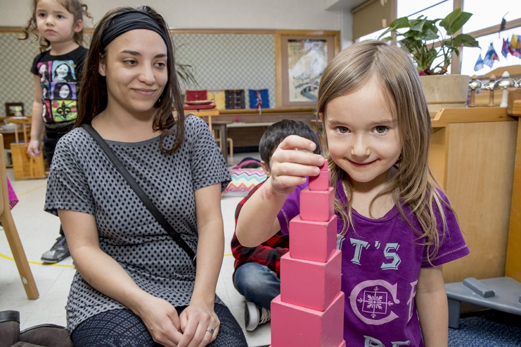 girl playing with building blocks while the teacher looks on